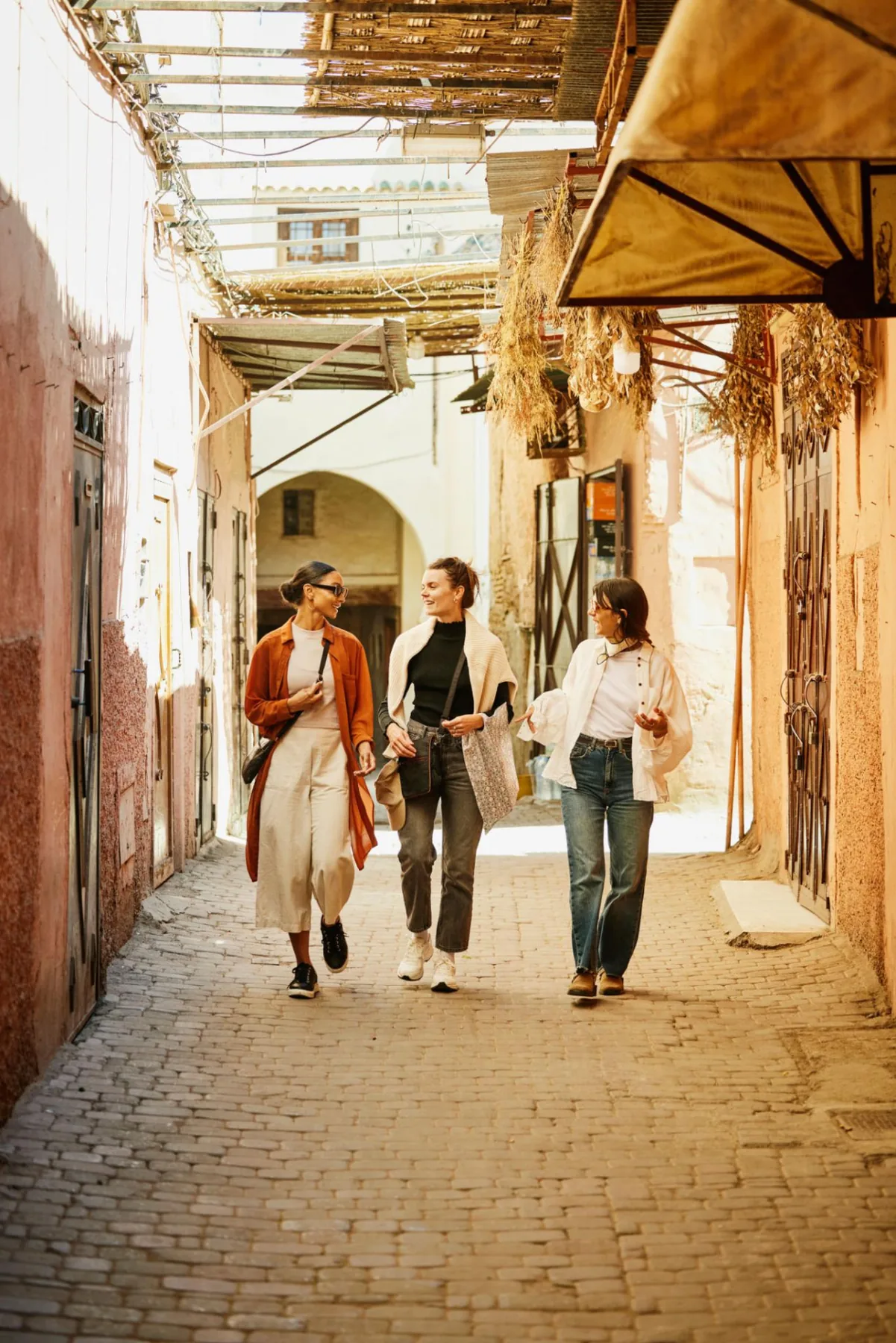 Tres amigas caminando por una callejuela soleada de la medina de Marrakech