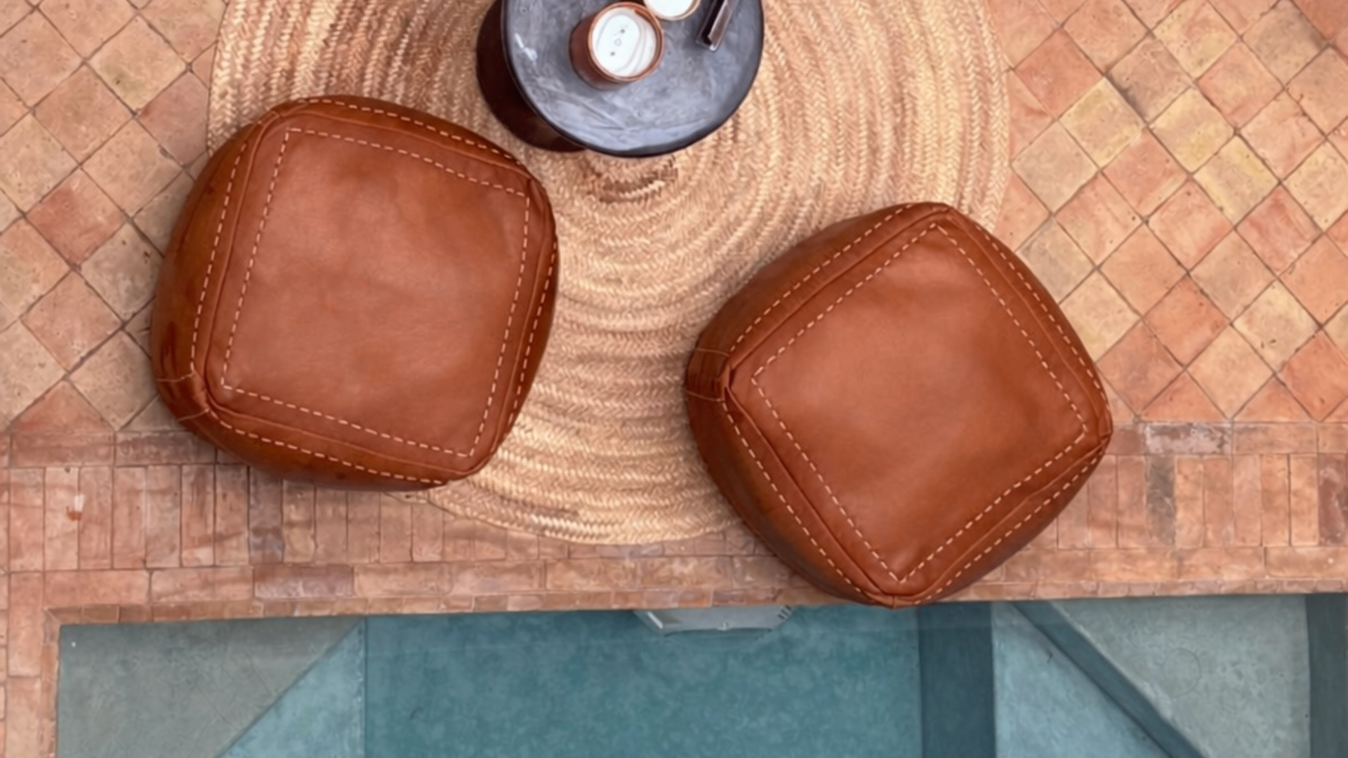 Poufs en cuir sur zellige terracotta au bord du bassin du patio du Riad Melqa